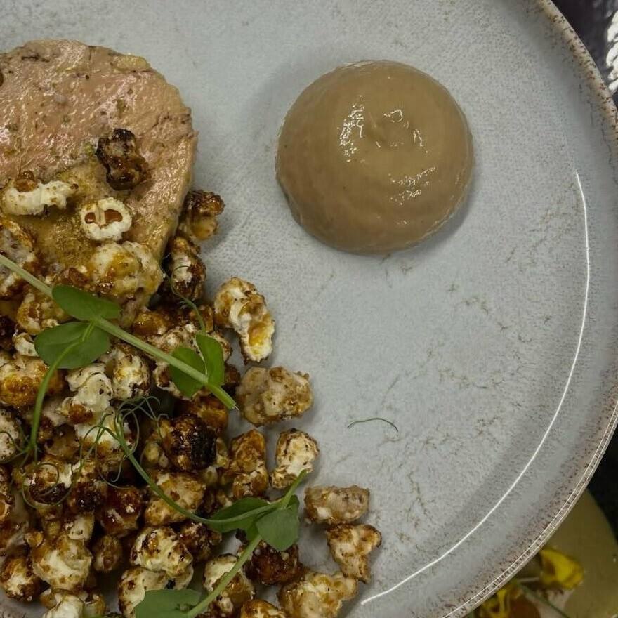 Tranche de terrine de foie gras, pop-corns épicés, jeunes pousses et dôme de chutney, sur une assiette gris clair.