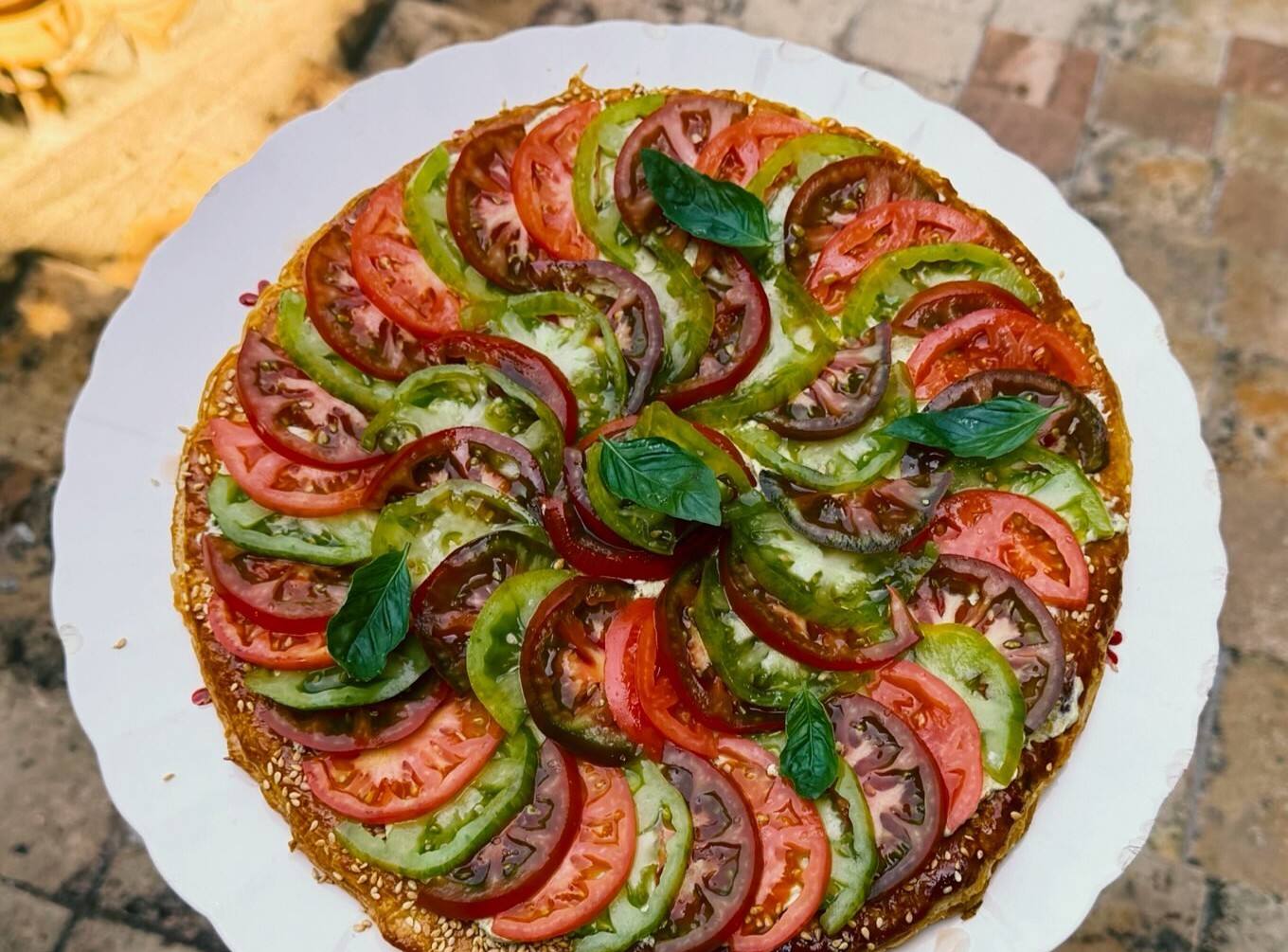 Tarte fine aux tomates rouges et vertes disposées en rosace, feuilles de basilic, vue du dessus.